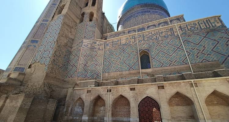 Nahaufnahme von kunstvollen blauen Mosaikfliesen und arabischer Kalligraphie an den Wänden eines antiken Mausoleums mit blauer Kuppel.
