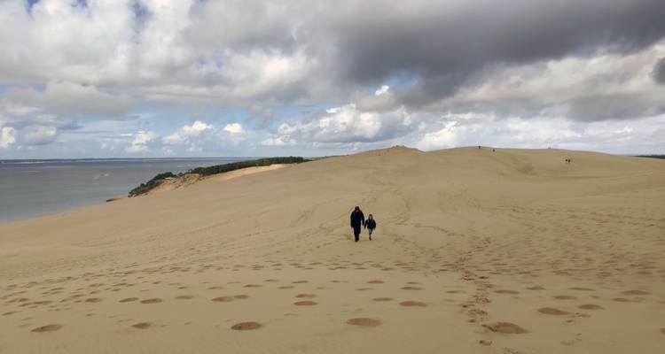 Ein Erwachsener und ein Kind wandern über den sanft ansteigenden Sand einer ausgedehnten Düne unter teilweise bewölktem Himmel.