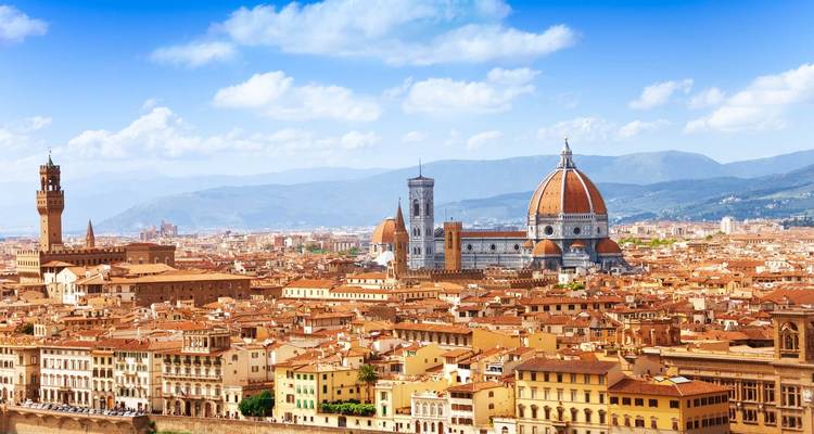 Vista panorámica de los tejados de terracota de Florencia con la icónica Catedral y las colinas circundantes bajo un cielo despejado.