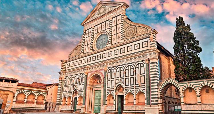 La fachada de mármol rayado de la Basílica di Santa Maria Novella brillando bajo un cielo al amanecer lleno de colores.