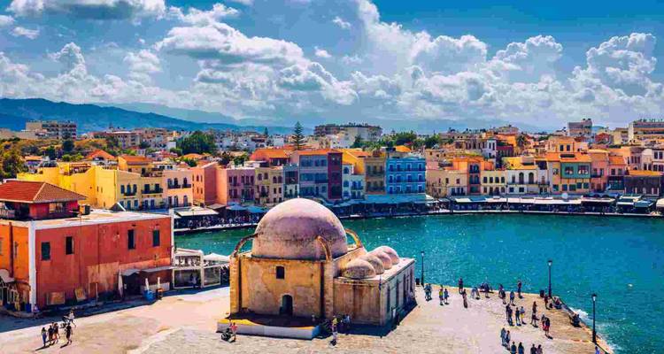 Farbenfrohe Hafengebäude und eine Moschee mit Kuppel, die einen lebhaften Hafen mit türkisblauem Wasser und verstreut umherwandelnden Besuchern überblickt.