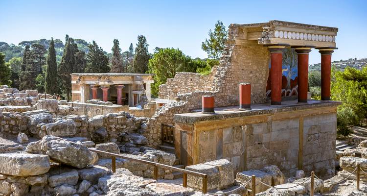 Goed bewaarde sectie van het Minoïsche Paleis in Knossos met rode zuilen omgeven door stenen ruïnes en cipressenbomen.