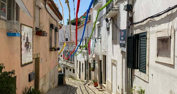 Narrow cobbled alley in Alfama decorated with colorful festival streamers under bright midday sun.