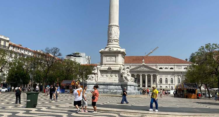 Rossio Square with the tall Dom Pedro IV column, patterned pavement and visitors strolling on a sunny day.