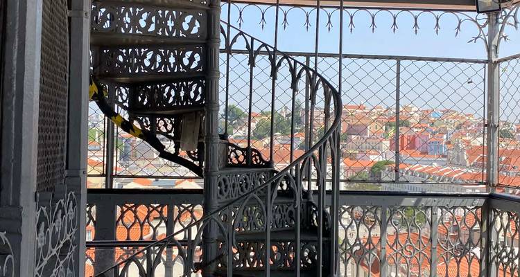 Cast-iron spiral staircase inside the Santa Justa Lift viewing platform framing Lisbon’s rooftops behind a safety mesh.