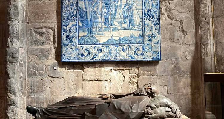 Stone tomb sculpture lies beneath a large blue-and-white azulejo tile panel inside a historic Lisbon monastery.
