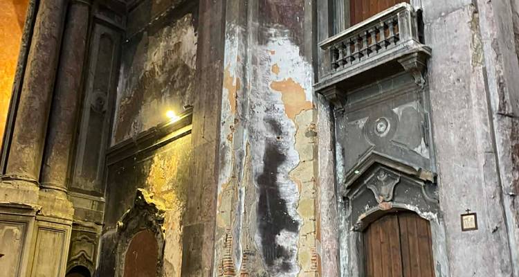Peeling plaster and weathered stone walls inside a historic Lisbon church illuminated by a single spotlight.