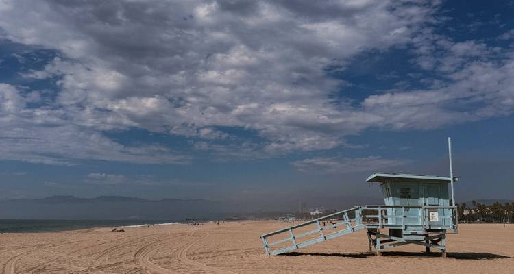 Tour de surveillance de plage bleu clair sur une large plage de sable sous des nuages épars.