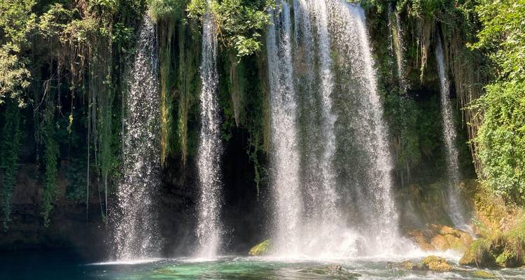 Exuberante cascada de Düden con múltiples niveles cayendo en una piscina de agua turquesa cristalina rodeada de vegetación.