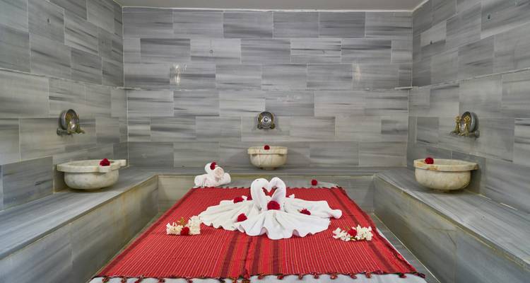 Lujosa sala de hammam en mármol gris con arte de toallas rojas con forma de cisnes y pétalos de rosa.