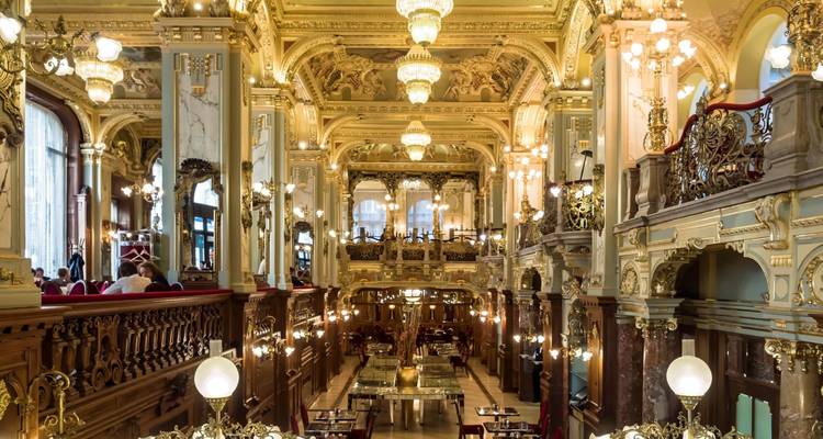 Interior de café histórico ornamentado con detalles dorados, arañas de cristal y balcones en Budapest