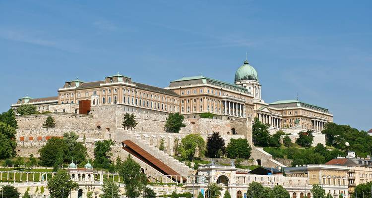 Vista amplia e iluminada por el sol del complejo del Castillo de Buda enmarcada por el cielo azul y la vegetación