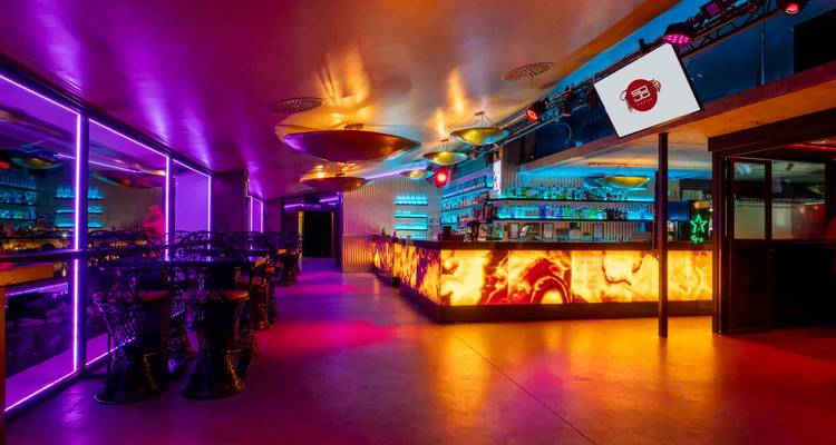 Un intérieur de bar élégant éclairé au néon avec un éclairage coloré et des bouteilles de spiritueux sur des étagères en verre.