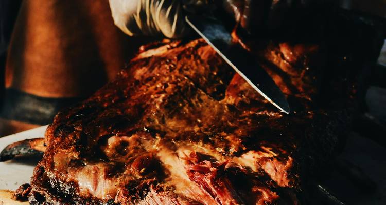 Gros plan sur du boeuf grillé en train d'être tranché par un chef portant des gants.