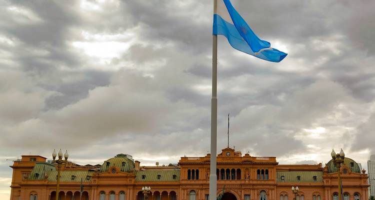 Le drapeau argentin flottant devant la Casa Rosada rose sous un ciel chargé.