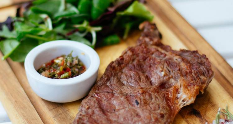 Plateau en bois avec steak grillé, salade d'accompagnement et chimichurri.