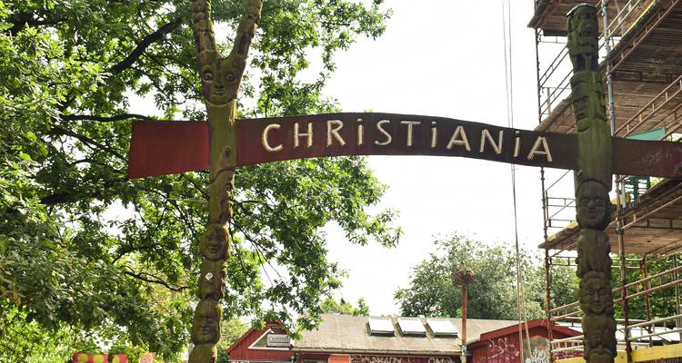 Arc d'entrée en bois portant l'inscription « CHRISTIANIA » avec des sculptures et un arrière-plan feuillu