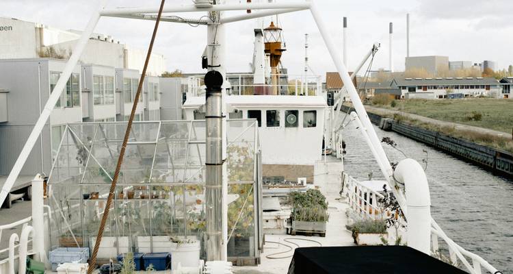Bateau de style industriel avec structures de serre amarré le long d'une voie navigable urbaine