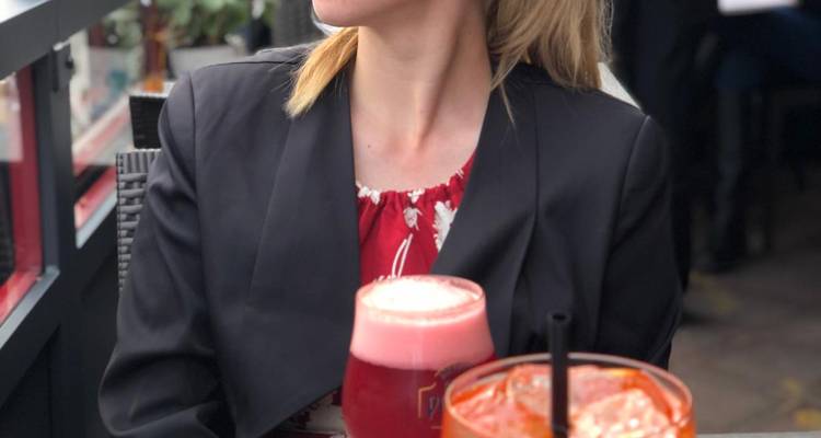 Jeune femme en blazer dégustant des boissons colorées à une table de café en plein air.