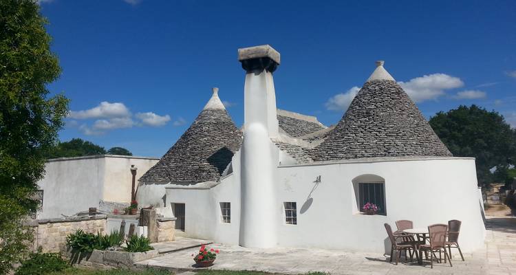 Complexe de maison trullo traditionnelle avec toits en forme de cône de pierre et murs blancs sous un ciel bleu éclatant