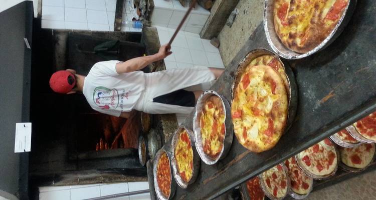 Boulanger utilisant une longue pelle pour glisser des plateaux de focaccia et de pizza dans un four à bois
