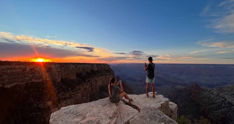 Deux voyageurs sont assis et photographient un coucher de soleil dramatique du Grand Canyon à partir d'une corniche rocheuse.