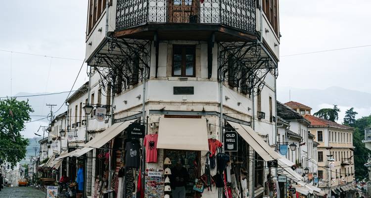 Historisches dreistöckiges Gebäude im ottomanischen Stil im Basar von Gjirokastra, vollgepackt mit Souvenirständen und hängenden Stoffen