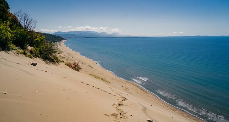 Ausgedehnte Küstensanddüne, die zu einem langen, leeren Strand und ruhigem blauen Meer mit fernen Bergen abfällt