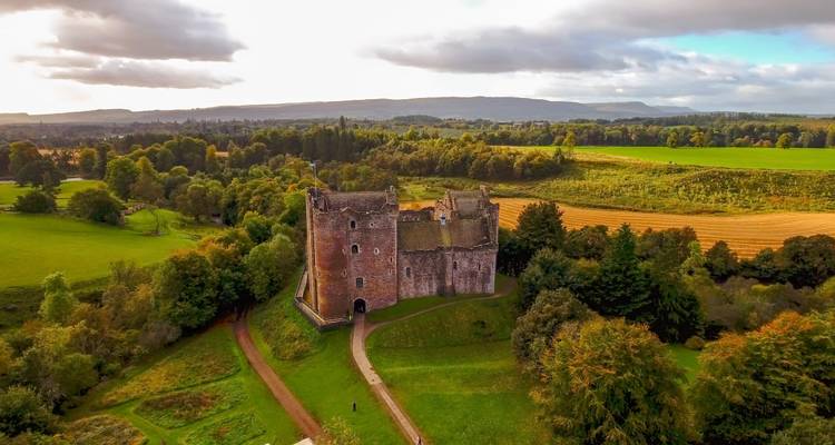 Vue aérienne spectaculaire du château de Doune entouré de forêts luxuriantes et de champs en patchwork au lever du soleil.