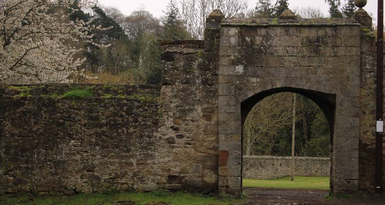 Entrée d'une arche en pierre usée par le temps dans un jardin écossais moussu par une journée grise.