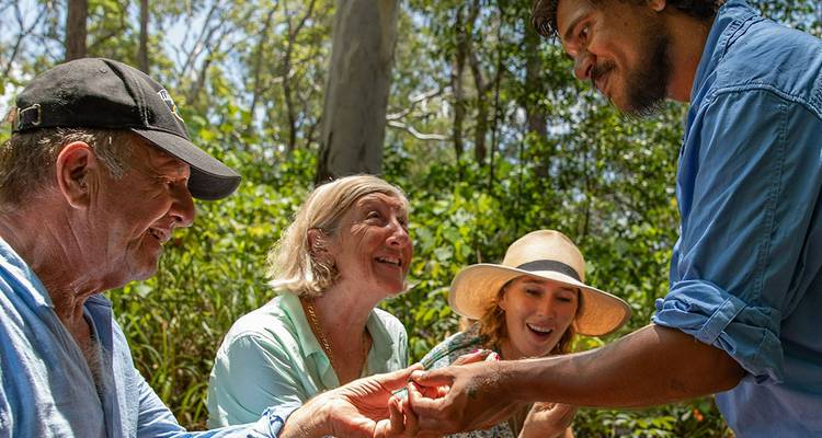 Een gids deelt bush tucker met een enthousiaste groep in een zonnige bosopen plek.