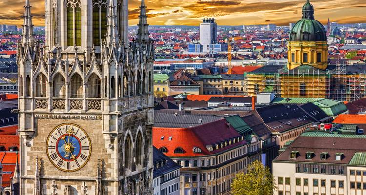 Erhöhte Ansicht der Münchener Skyline mit dem Uhrturm des Neuen Rathauses und der Kuppel der Theatinerkirche bei Sonnenuntergang
