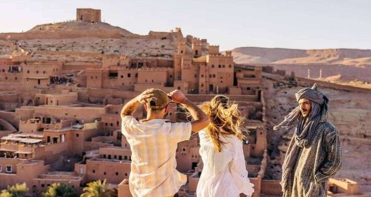 Reizigers en een lokale gids bewonderen het oude klei fort van Ait Benhaddou vanaf een heuvel.