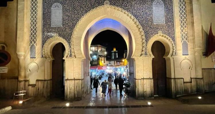 Nachtscène van de sierlijke blauwtegels Bab Bou Jeloud-poort die uitgeeft op een drukke straatje in de medina