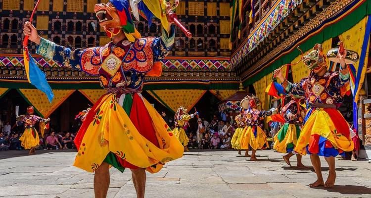 Farbenfrohe maskierte Tänzer in aufwendigen Kostümen führen ein traditionelles Festival in einem Klosterhof auf.