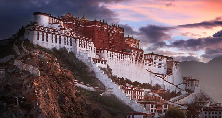 Le Palais du Potala perché sur une colline rocheuse illuminée par les couleurs dramatiques du coucher de soleil et des nuages d'humeur changeante.