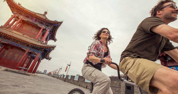 Les cyclistes passent devant une tour chinoise traditionnelle sur un mur d'enceinte d'une ville historique.