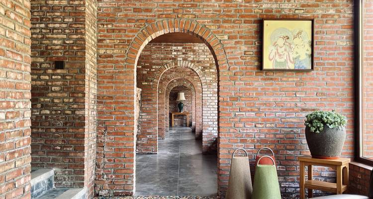 Série d'arcades en brique formant un motif de couloir répétitif avec des œuvres d'art et des plantes en pot.
