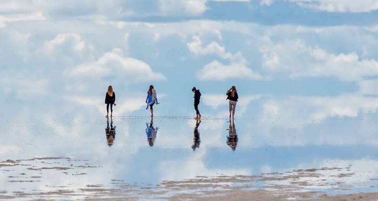 Quatre voyageurs marchant à travers les vastes étendues de sel d'Uyuni aux surfaces miroir qui reflètent le ciel