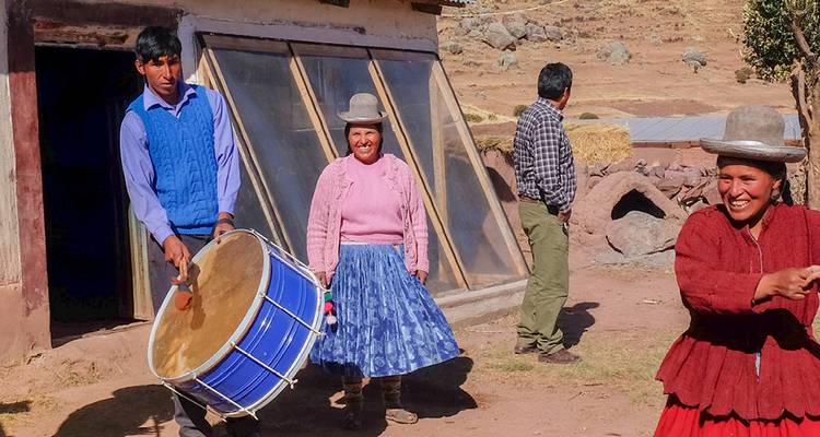 Locals in traditional Andean clothing outside an adobe house, one playing a large drum.