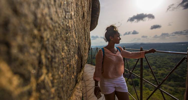 Un viajero hace una pausa en una estrecha cornisa de la Fortaleza de Roca de Sigiriya con vistas al exuberante bosque de Sri Lanka.