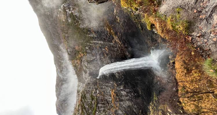 Puissante cascade verticale se précipitant dans une gorge remplie de brume au milieu du feuillage automnal et des falaises.