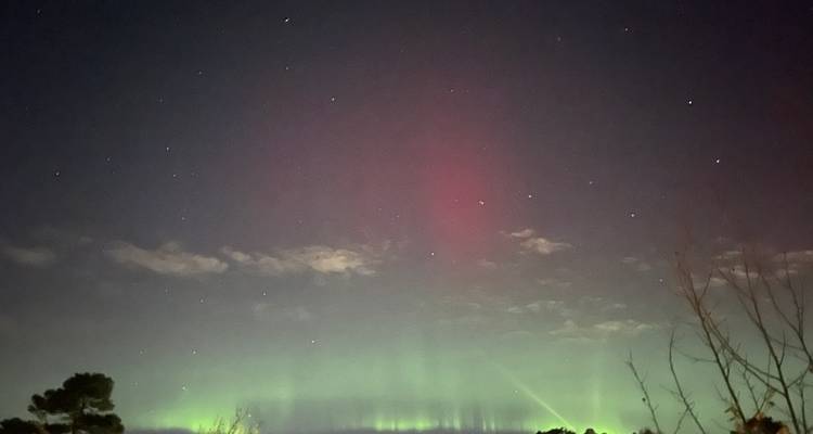Ciel nocturne avec des bandes faibles d'aurores boréales vertes et rouges et des étoiles dispersées au-dessus d'un horizon sombre.