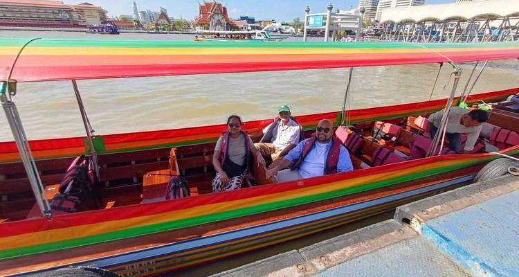 Des voyageurs assis dans un bateau à longue queue coloré sur la rivière Chao Phraya avec des temples de Bangkok en arrière-plan.