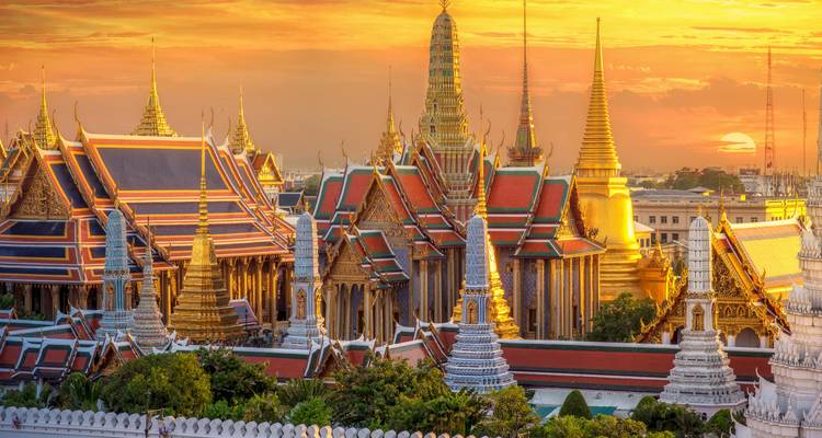 Les toits dorés du Wat Phra Kaew brillent au coucher du soleil sur un ciel orange éclatant à Bangkok.