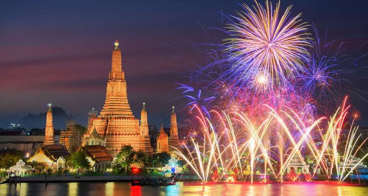 Des feux d'artifice colorés éclatent au-dessus du temple illuminé de Wat Arun se reflétant sur le fleuve la nuit.
