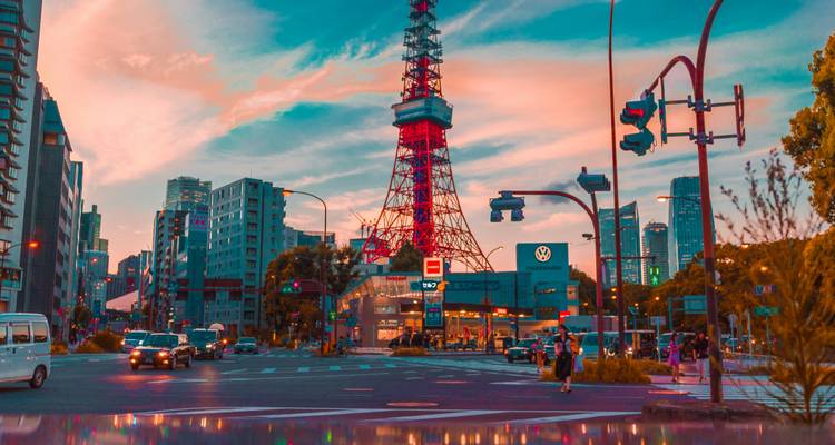 Straßenszene bei Sonnenuntergang mit Autos, Fußgängern und dem rot beleuchteten Tokyo Tower, der sich gegen einen farbenfrohen Himmel erhebt.