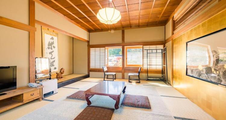 Habitación japonesa de estilo tatami tradicional con mesa de madera baja, cojines de piso y ventanas shoji.