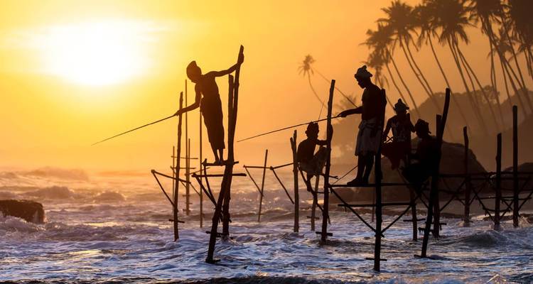 Des pêcheurs sur échasses se détachant en silhouette s'équilibrent au-dessus des vagues lors d'un coucher de soleil tropical resplendissant.