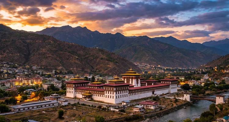 Panoramischer Blick in der Abenddämmerung über das Thimphu-Tal mit dem majestätischen, vor einer Bergkulisse illuminierten Tashichho Dzong